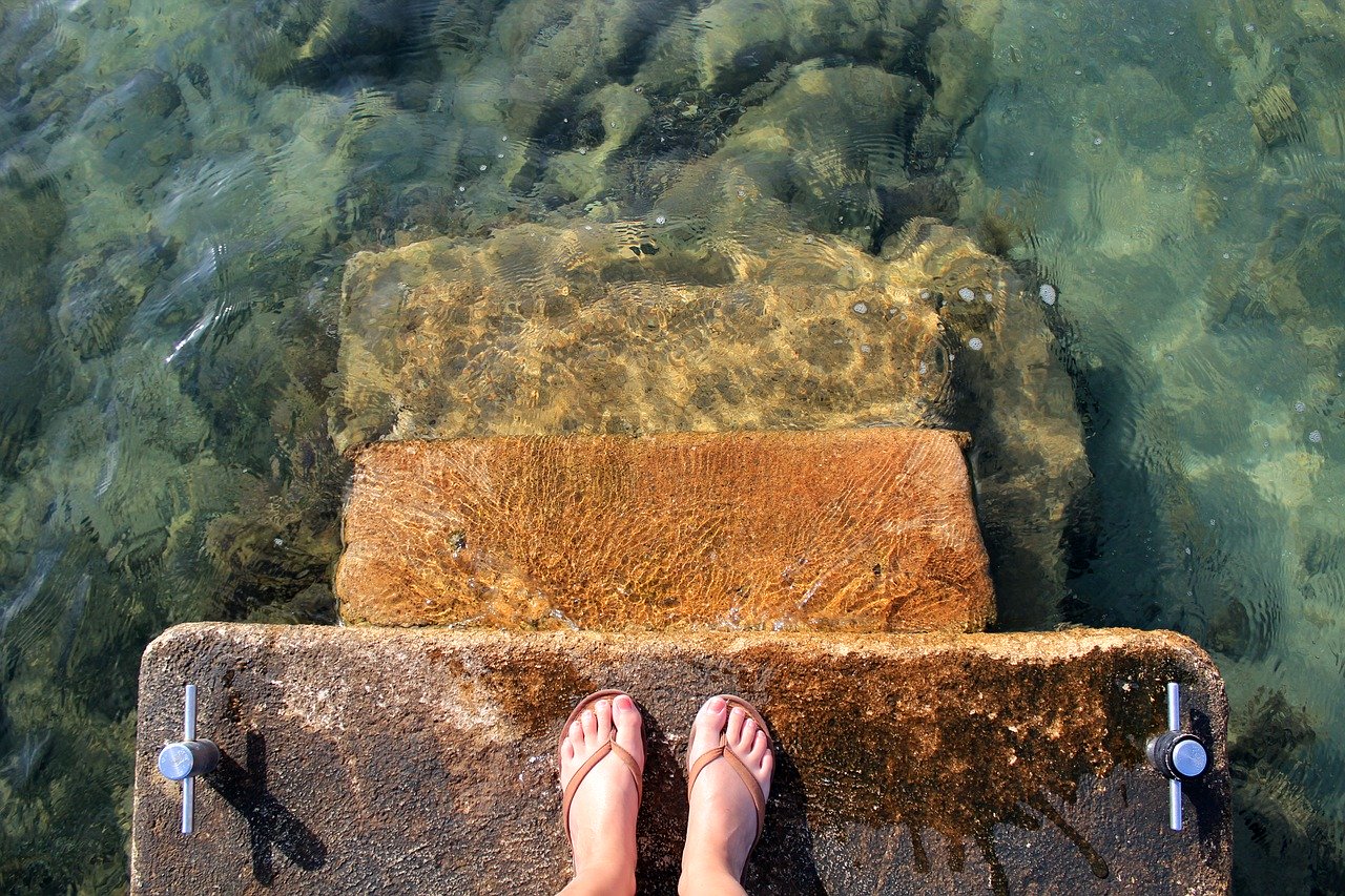 A top view of woman's feet on rustic stone steps into the sea