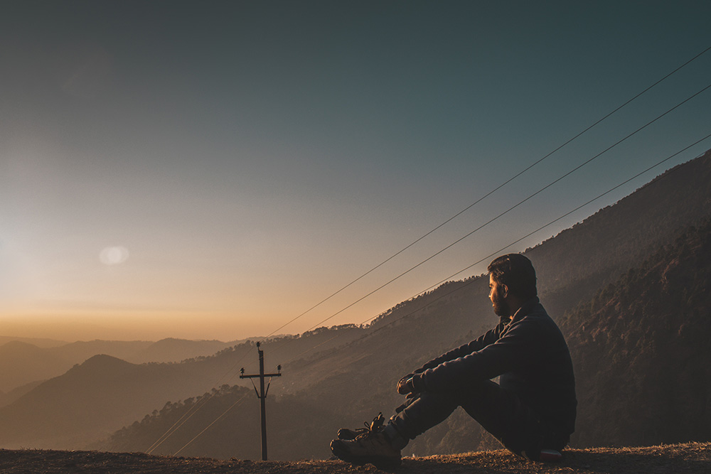 Man sitting on hill facing sunrise
