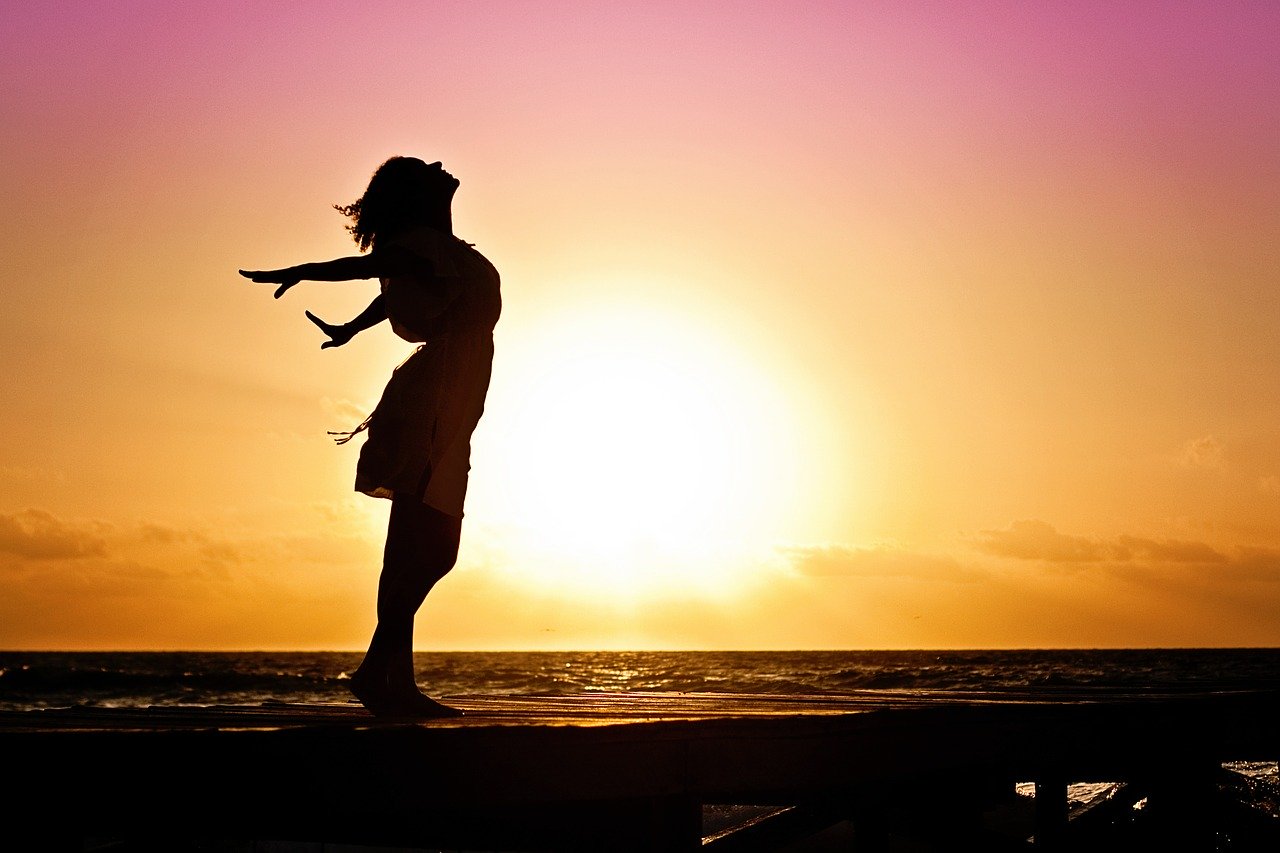 A silhouette of a woman with pink and orange hue of the sunrise