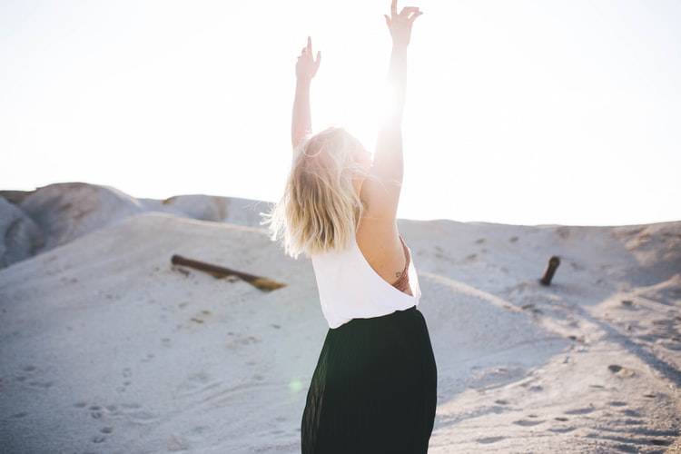 A woman standing on a desert-like ground with hands raised up