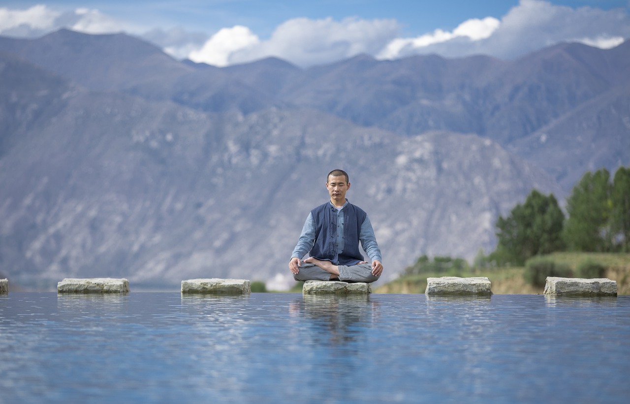 A man sitting on top of a stepping stone above water