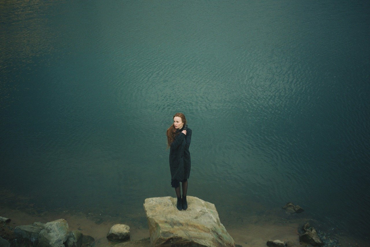 A woman standing on a small flat rock in the middle of a body of water