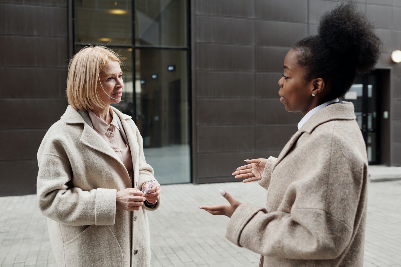 A female caucasian and a black american female talking outside a corporate building