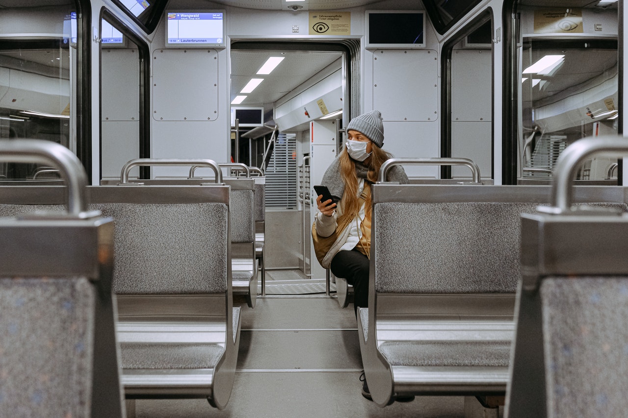 A lady sitting on a train alone with a face mask
