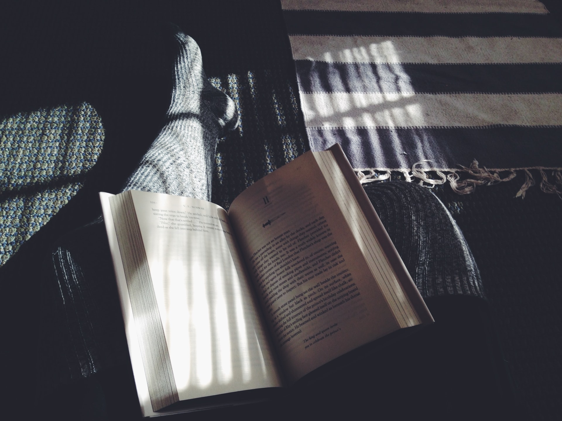 A person reading a book on the floor with a ray of sunshine coming in from a window