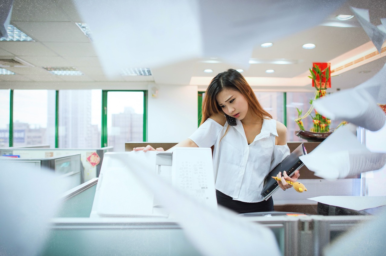 A female on the phone in front of a copying machine and papers flying in the background