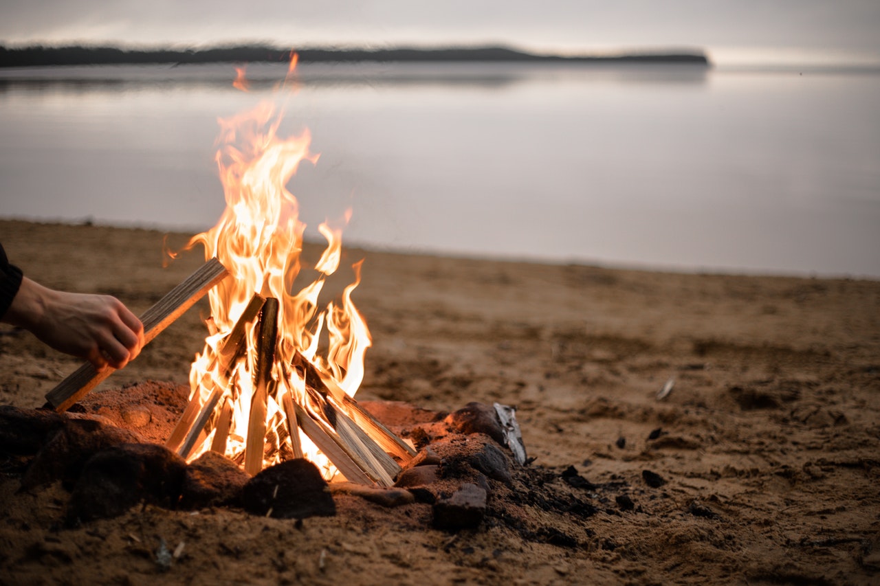 A bonfire on brown sand near a lake